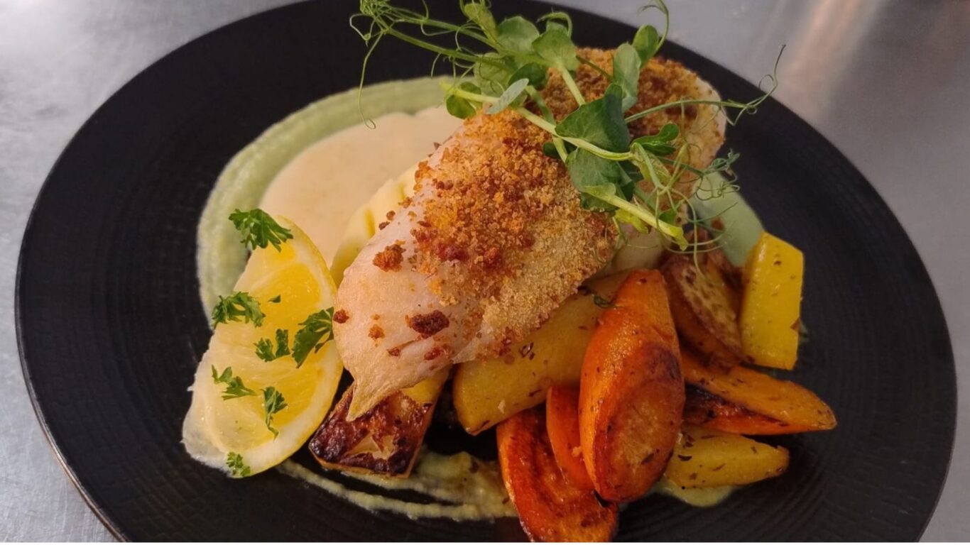 Elegant dish of herb-crusted fish with vibrant roasted vegetables and lemon garnish at luxury hotel dining experience.