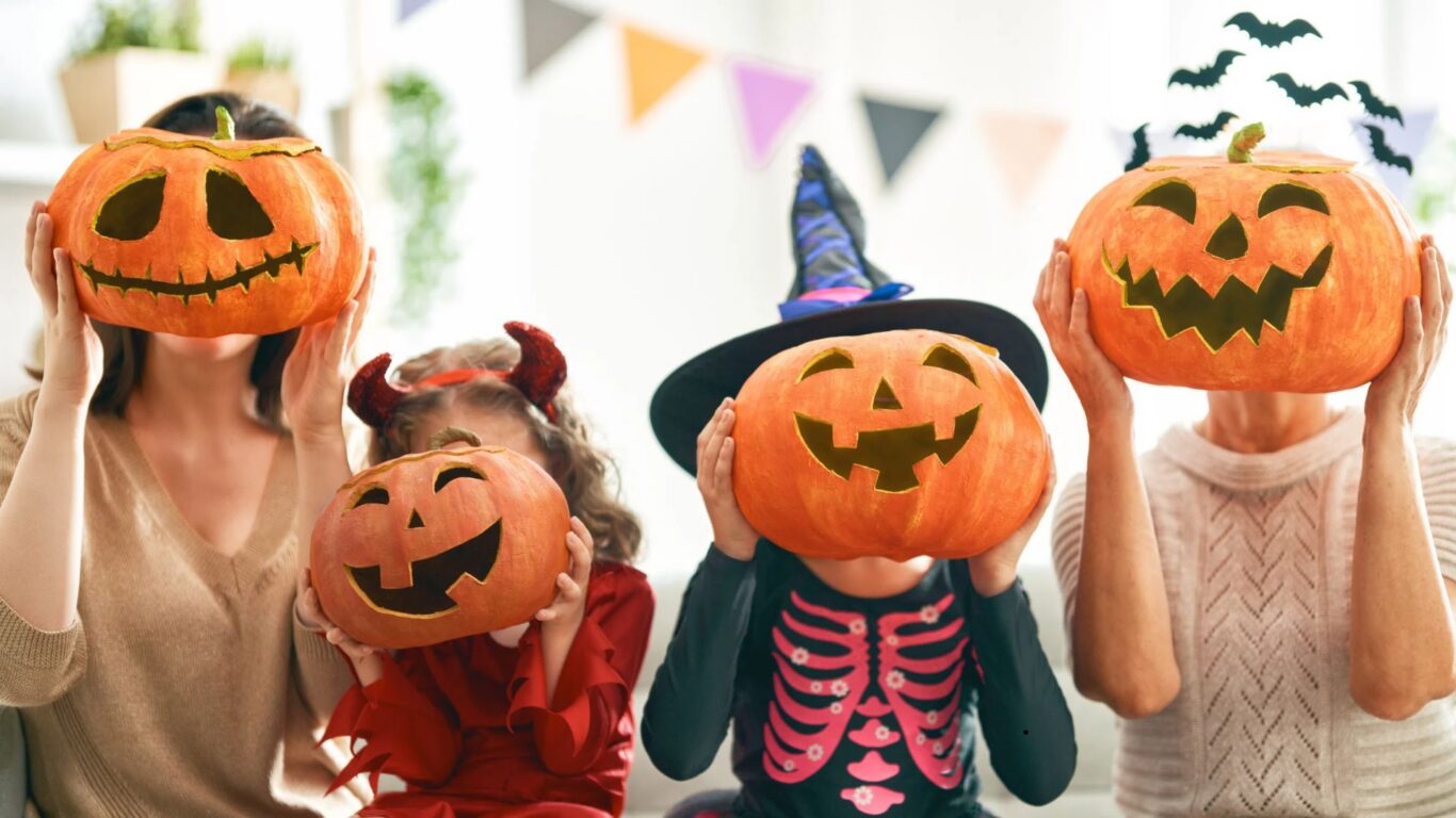 Family enjoying Halloween fun with carved pumpkins, festive decorations in bright hotel room.