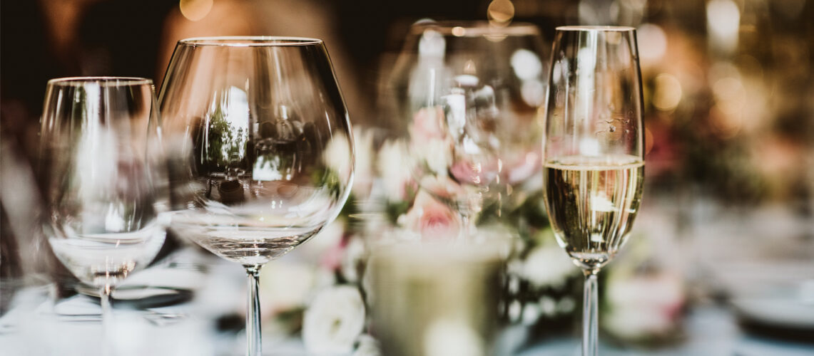 Close-up of empty wine glasses and a filled champagne flute on a table with blurred floral decorations in the background.