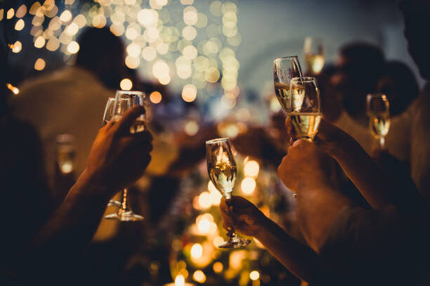 A group of people raise champagne glasses in a toast at a dimly lit gathering, with blurred lights and candles in the background.