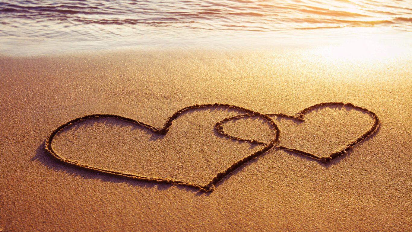 Two overlapping hearts are drawn in the sand on a beach at sunset, with gentle waves in the background—perfect inspiration for romantic escapes or Valentines hotel deals Wexford couples will love.