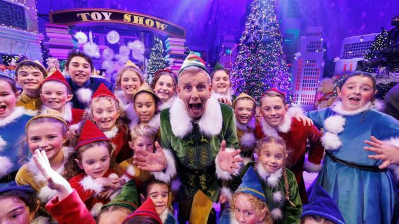 Joyful children in festive costumes with vibrant Christmas lights and tree, creating a magical holiday show experience.