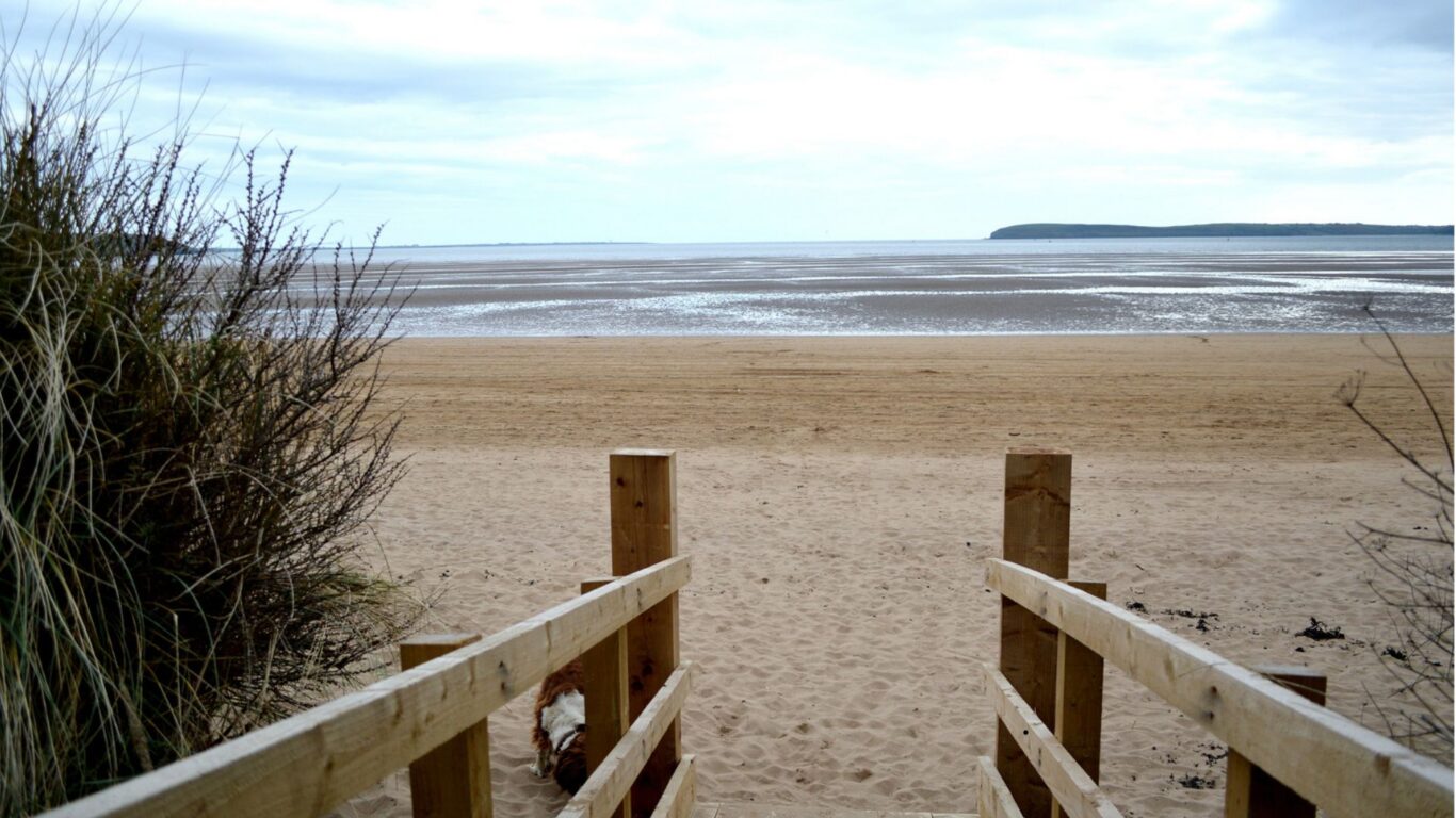 Wooden walkway leading to serene sandy beach with sea views, perfect for relaxation at coastal hotel retreat.